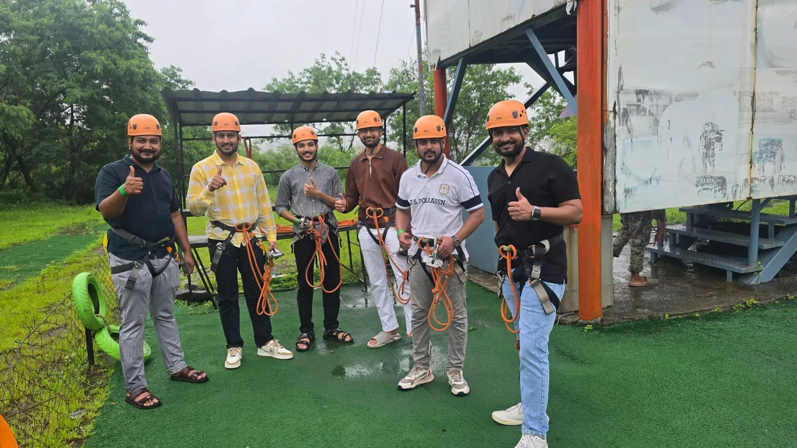 Team members in orange helmets and climbing harnesses giving a thumbs up before an activity
